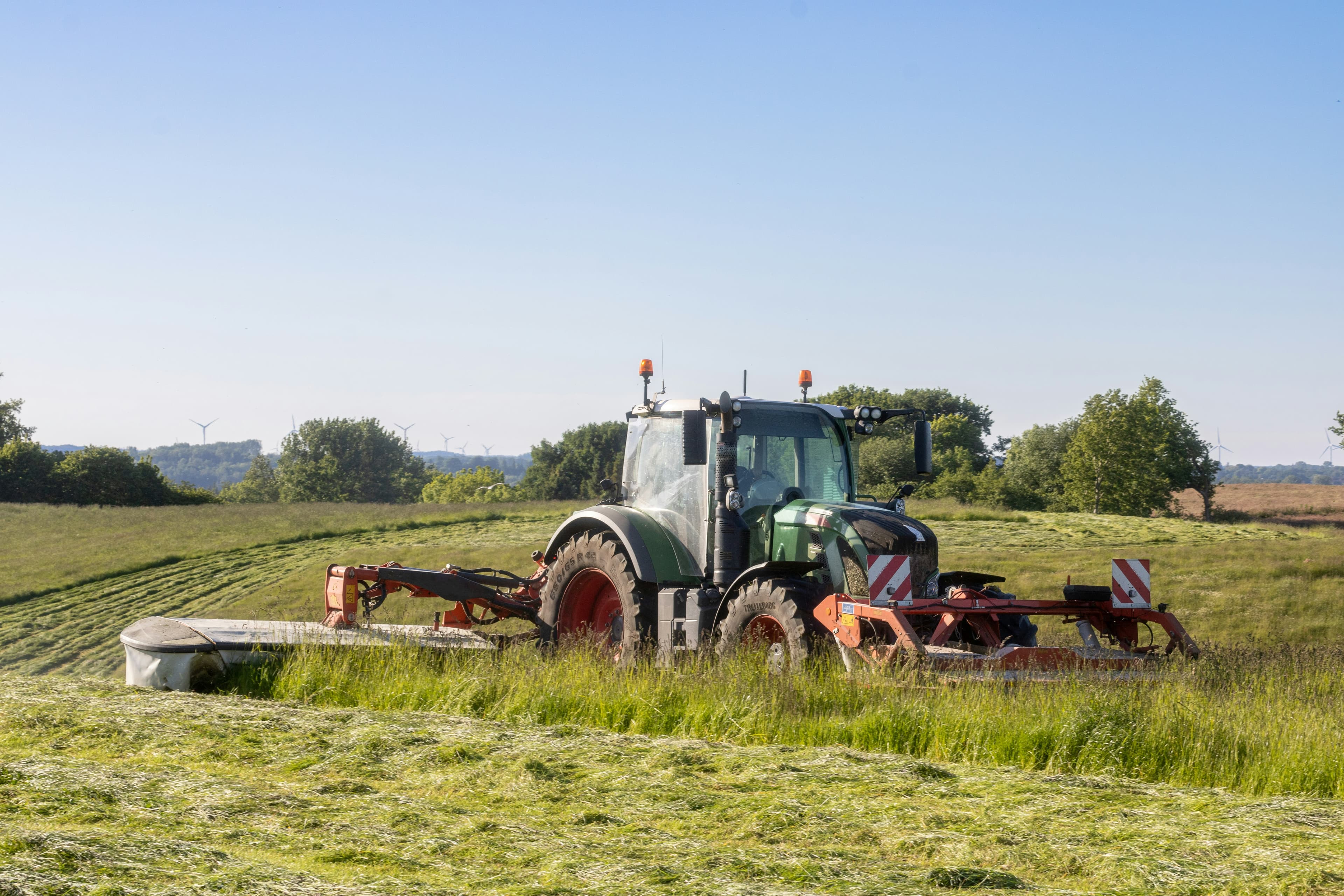 Tractor segando un prado verde bajo el sol.